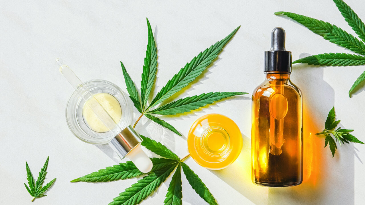 Glass brown bottle with cannabis CBD oil and hemp leaves on a marble background. Copy space