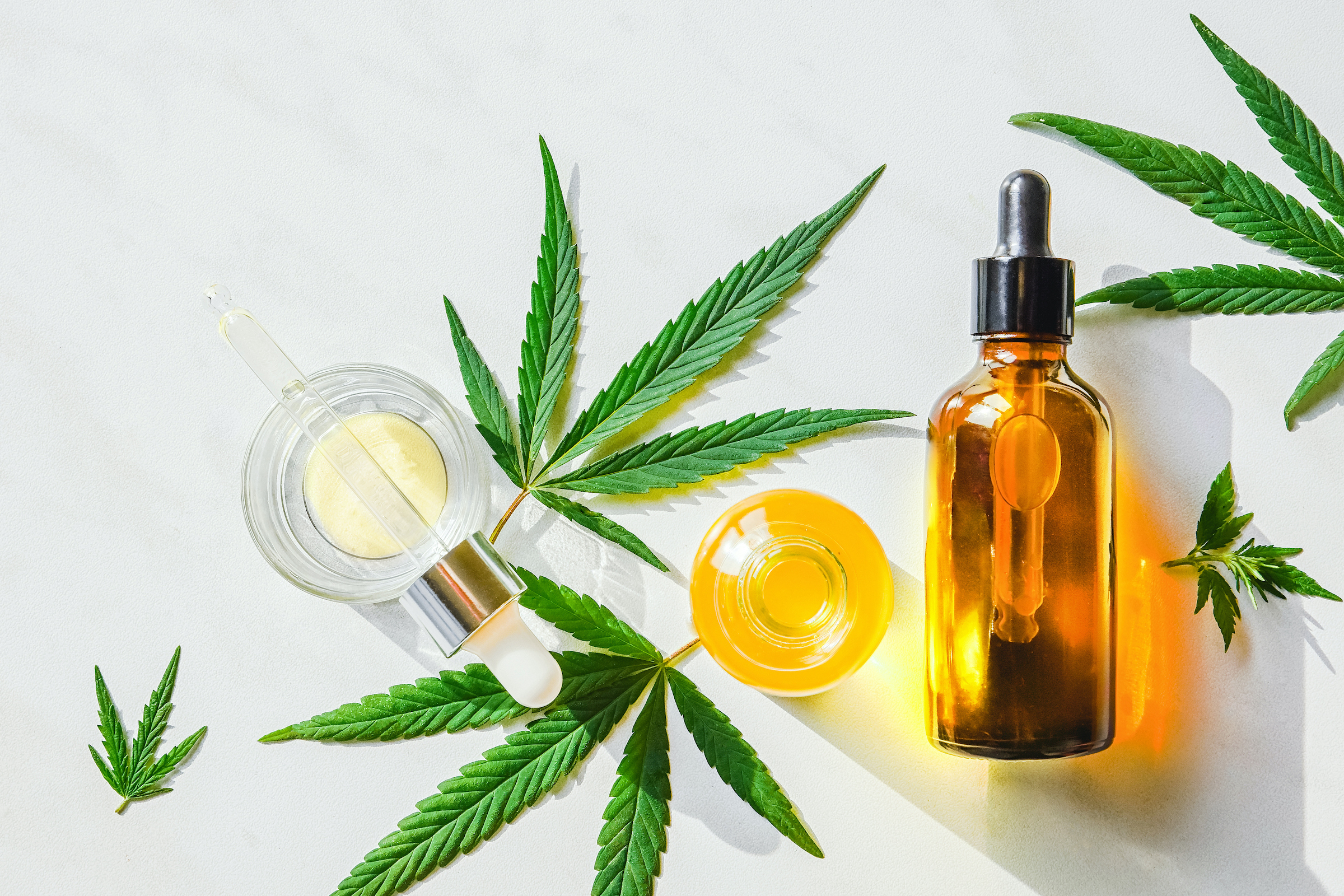 Glass brown bottle with cannabis CBD oil and hemp leaves on a marble background. Copy space